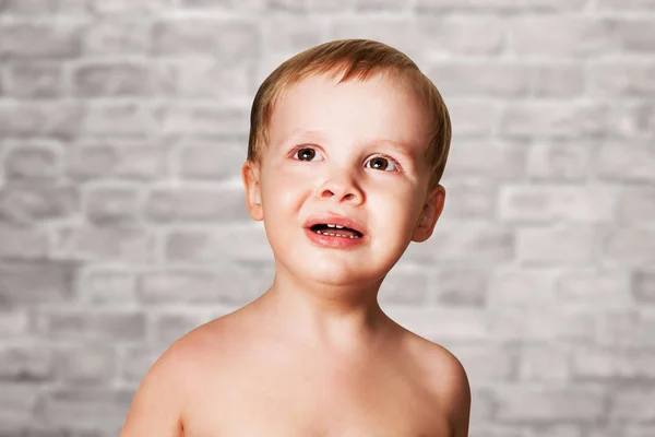 Bonito criança insatisfeita chorando, no fundo da parede de tijolo — Fotografia de Stock