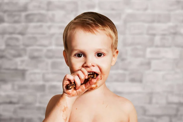 Bonito criança manchado rosto no chocolate no tijolo parede fundo — Fotografia de Stock