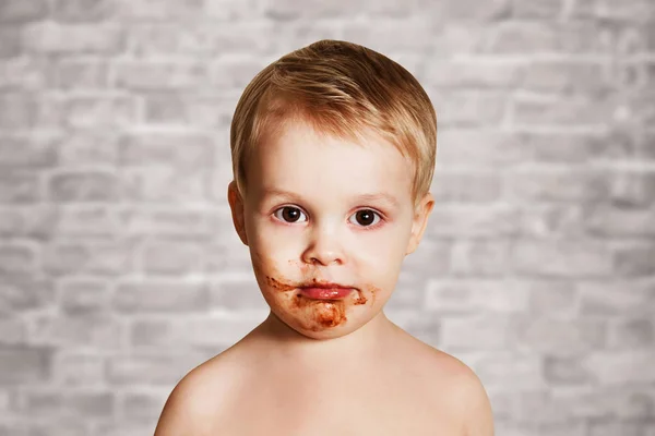 Söt barn utsmetad ansikte i choklad på tegelvägg bakgrund — Stockfoto