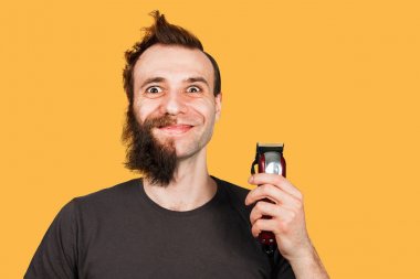 Man with half shave beard surprised with wide eyes hold hair clipper. Isolated on orange background clipart
