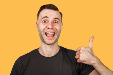 Genç adam baş parmağını kaldırıyor ve gülümsüyor. Turuncu arka planda izole edilmiş
