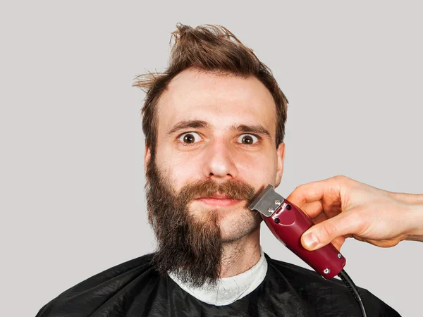 Homem na barbearia corta sua barba com aparador em fundo cinza . — Fotografia de Stock