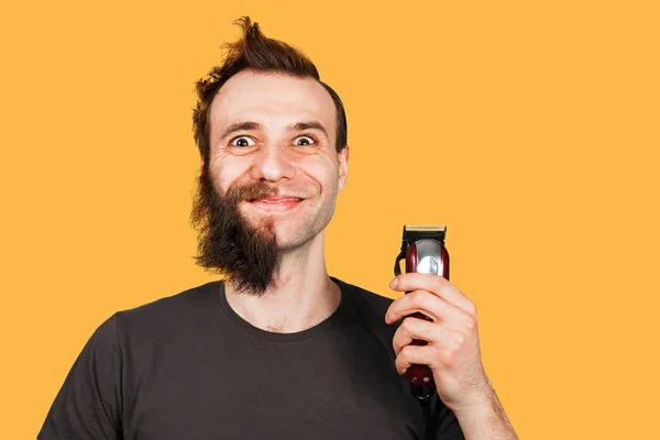 Yarım tıraş sakallı adam geniş gözlü saç makasını tutar. Turuncu arka planda yalıtılmış — Stok fotoğraf