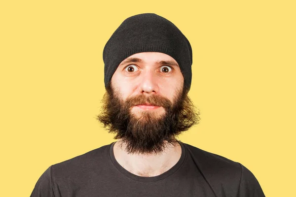 Joven con barba en sombrero mira en cámara de ojos anchos. Aislado sobre fondo amarillo — Foto de Stock