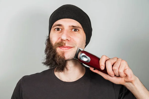 Jonge man in hoed met half geschoren zijn baard op grijze achtergrond. — Stockfoto