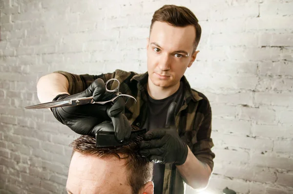 Перукар розрізає волосся і розчісує дорослого чоловіка на фоні цегляної стіни. Крупним планом портрет хлопця — стокове фото