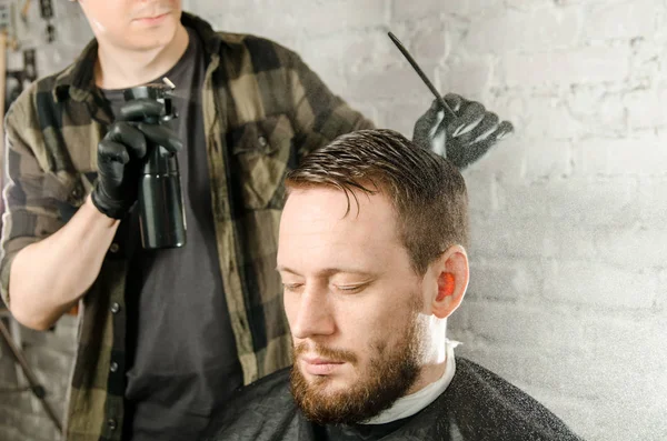 Barber saupoudrer l'eau des cheveux pulvérisateur et peigne homme adulte sur un fond de mur de briques. Gros plan portrait d'un gars — Photo