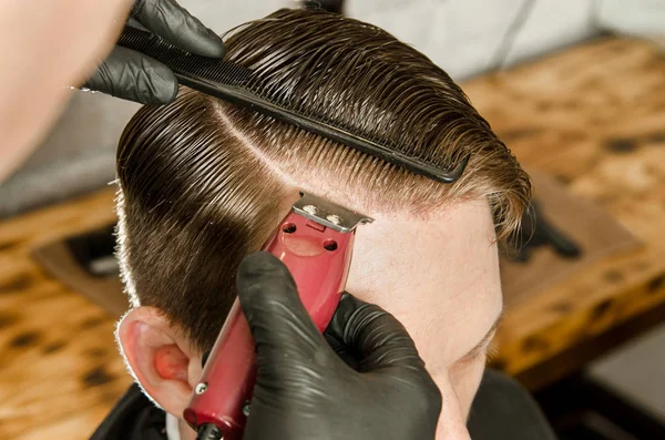 Friseur schneidet Haare und rasiert den scheidenden erwachsenen Mann vor Backsteinmauer-Hintergrund. Nahaufnahme Porträt eines Mannes — Stockfoto