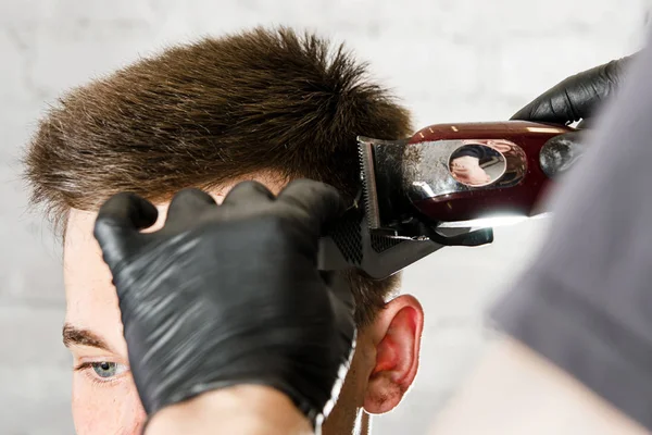 Barbeiro cortar cabelo e pentear o homem adulto em um fundo de parede de tijolo. Close up retrato de um cara — Fotografia de Stock