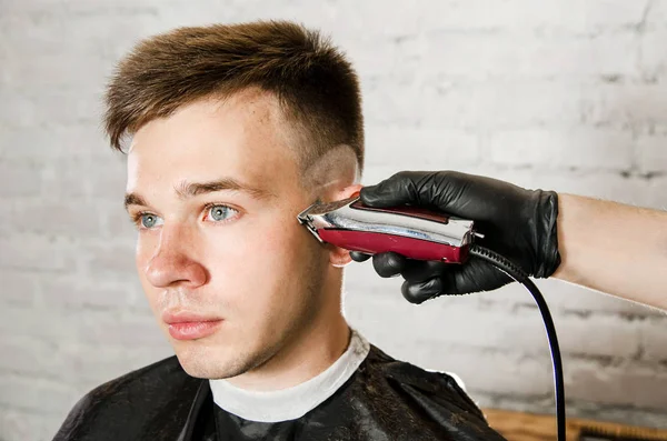 Barbier main dans des gants couper les cheveux et se rase jeune homme sur un fond de mur de briques. Gros plan portrait d'un gars — Photo