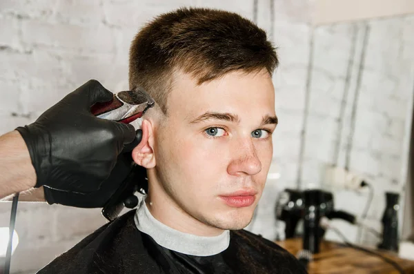 Barbier main dans des gants couper les cheveux et se rase jeune homme sur un fond de mur de briques. Gros plan portrait d'un gars — Photo