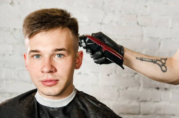 Friseurhand in Handschuhen schneidet Haare und rasiert jungen Mann vor Backsteinmauer-Hintergrund. Nahaufnahme Porträt eines Mannes — Stockfoto