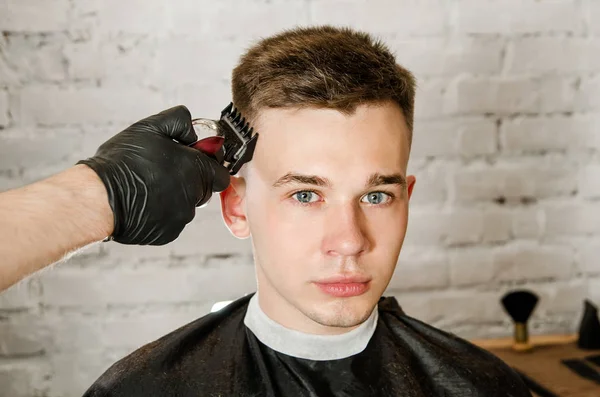 Barbier main dans des gants couper les cheveux et se rase jeune homme sur un fond de mur de briques. Gros plan portrait d'un gars — Photo
