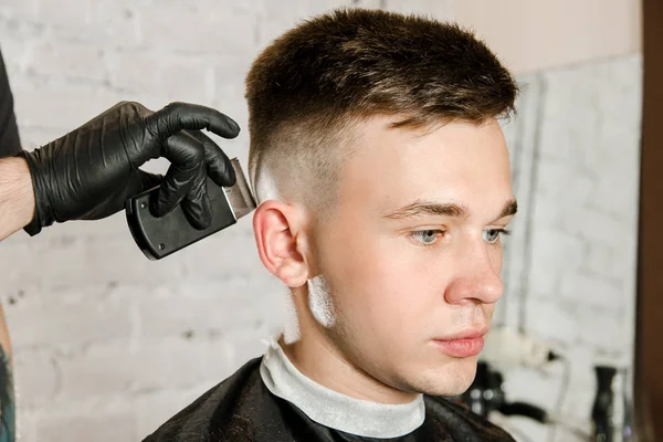 Barbier main dans des gants couper les cheveux et se rase jeune homme sur un fond de mur de briques. Gros plan portrait d'un gars — Photo