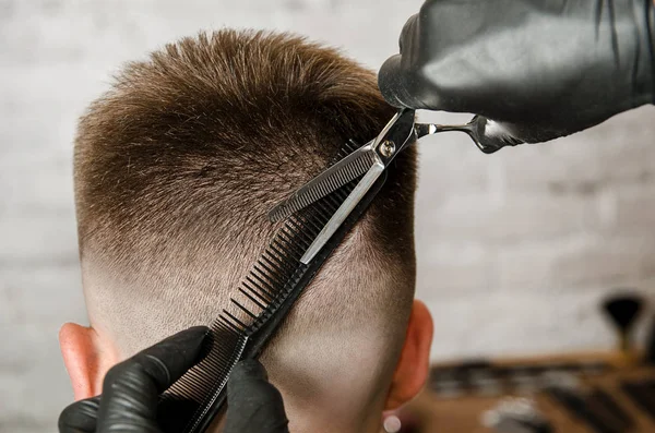 Barbier main dans des gants couper les cheveux et se rase jeune homme sur un fond de mur de briques. Gros plan portrait latéral d'un gars, vue de dos — Photo