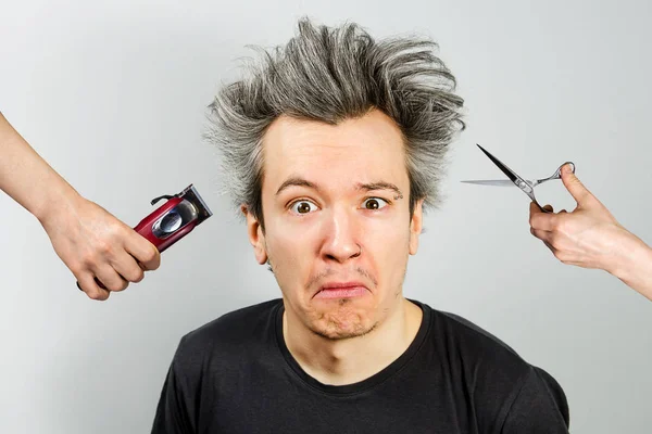 Hand with clipper and hand with scissors cut overgrown unshaven guy with on a gray background — Stock Photo, Image