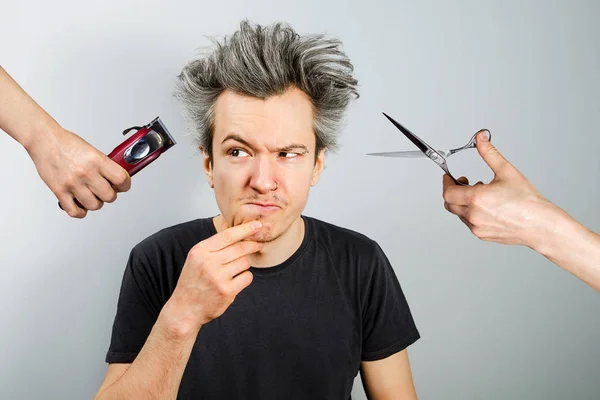 Hand with clipper and hand with scissors cut overgrown unshaven guy with on a gray background — Stock Photo, Image