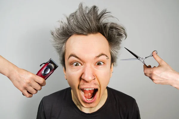 Hand with clipper and hand with scissors cut overgrown unshaven guy with on a gray background — Stock Photo, Image