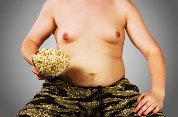 Body fiatal férfi a túlsúly, tartsa hasa zsírt pattogatott kukoricát, a szürke háttér. — Stock Fotó