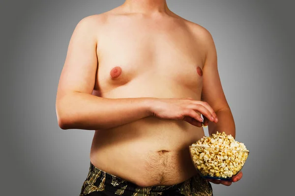 Тіло молодого чоловіка з надлишковою вагою, тримайте жир на животі з попкорном, на сірому фоні . — стокове фото
