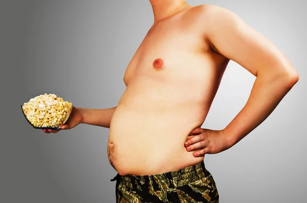 Cuerpo de hombre joven con exceso de peso, mantener la grasa del vientre con palomitas de maíz, sobre un fondo gris . —  Fotos de Stock