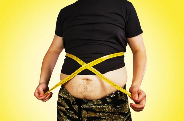 과체중을 가진 젊은 남자의 몸, T 셔츠에 배꼽 지방을 유지, 노란색 배경에 측정 테이프로 자신을 측정. — 스톡 사진