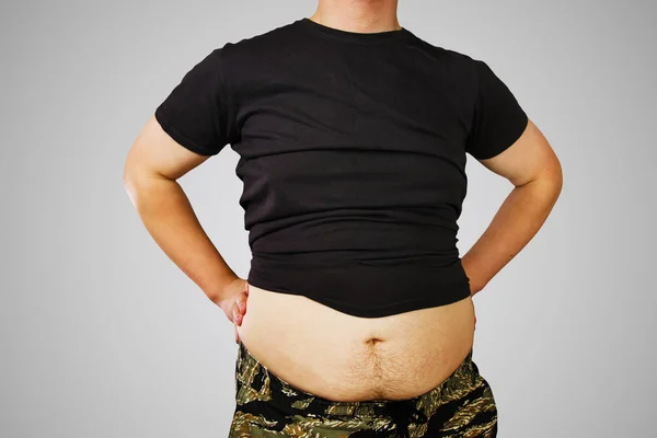Body av ung man med övervikt, hålla magen fett i en t-shirt, på grå bakgrund. — Stockfoto