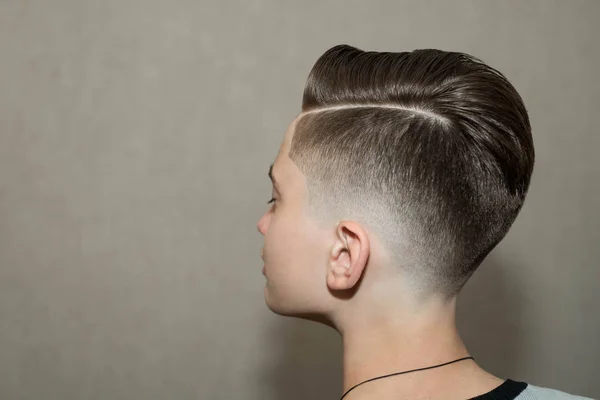 Elegante moderno corte de pelo retro parte lateral con mediados se desvanecen con la despedida de un chico de la escuela en una barbería sobre un fondo marrón —  Fotos de Stock