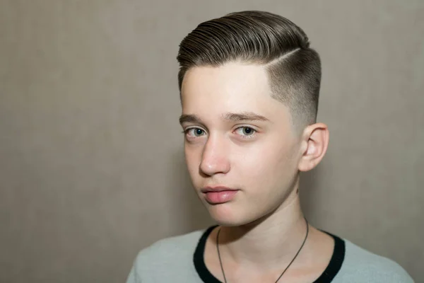 Corte de cabelo moderno elegante parte lateral retro com desbotamento médio com a separação de um menino da escola em uma barbearia em um fundo marrom — Fotografia de Stock