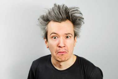 Tıraşsız, uzun saçlı, rencide olmuş ve gri arka planda olgunlaşmış bir adam.