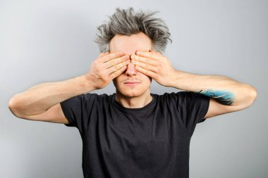 Young white caucasian guy with gray hair cover his eyes hands on a gray background clipart