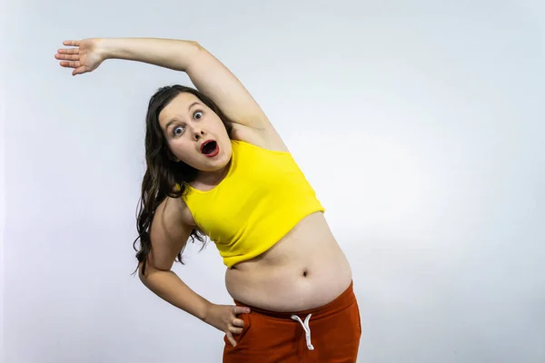 young fat happy woman in sportswear is engaged in sports on a stretch: makes slopes in the side. body positivity concept.