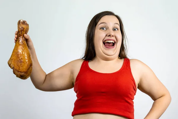fat woman with double chin and excess weight, laugh and holds a large chicken leg.