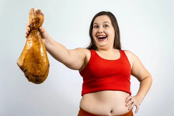 fat girl with double chin and excess weight, smiles and holds a large chicken leg.