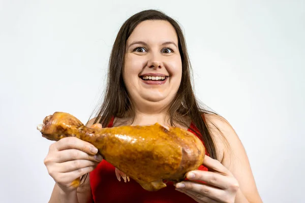 fat happy woman with double chin and excess weight, smiles and holds a large chicken leg.
