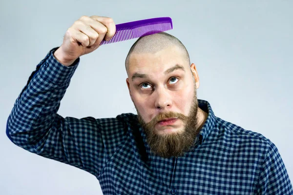 Portrait of sad bearded bald man hold comb in his hand. The concept of hair loss and hair transplantation