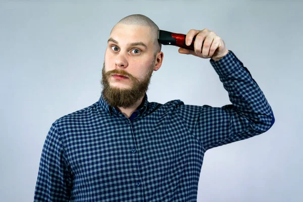 Portrait of bearded bald man holding trimmer, in his hand. The concept of hair loss and hair transplantation