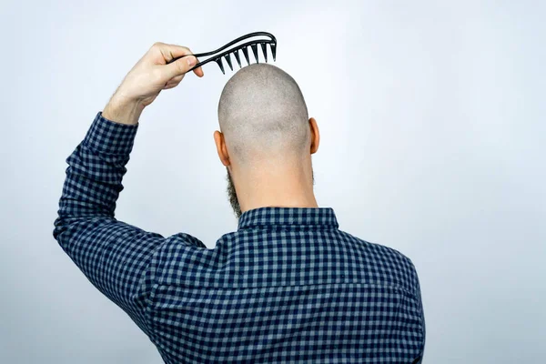 Portrait of back bald man head holding a comb in his hand. The concept of hair loss and hair transplantation