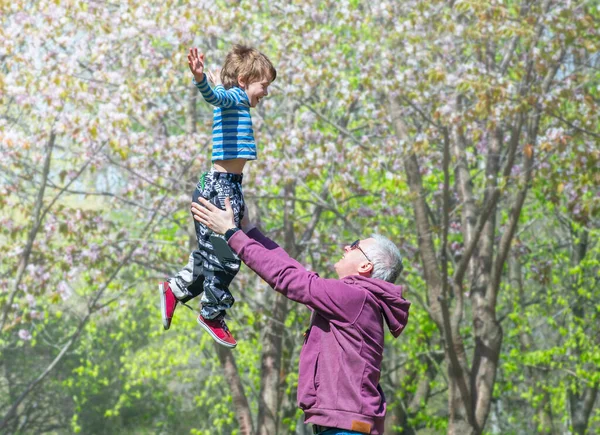 Pai feliz e filho pequeno. Papai joga seu filho contra o fundo de árvores floridas . — Fotografia de Stock