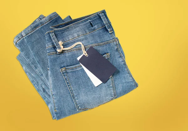 Pantalón vaquero plegado azul claro con etiqueta azul sobre fondo amarillo . — Foto de Stock