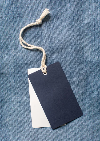 Blue and white clothing tag on a denim background. Label blank mockup template at blue jeans background.