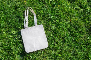 Uzun saplı beyaz bir bez çanta yeşil çimlerin üzerinde yatıyor..