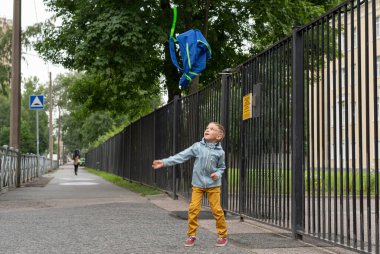 Bir okul çocuğu okul binasının yanına bir sırt çantası fırlatıyor. Okula geri dön..