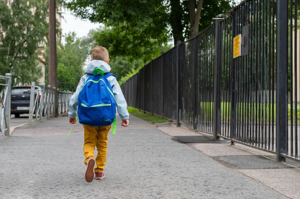 En liten pojke med blå väska ska till skolan. Ett barn går i grundskolan första gången. Tillbaka till skolan. — Stockfoto