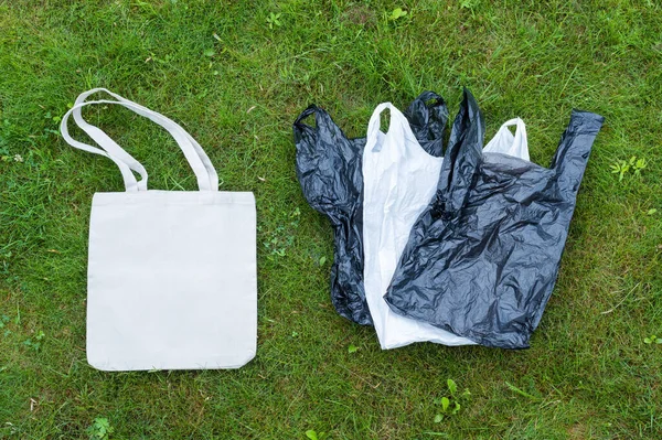 One textile bag against many single-use plastic bags. The concept of zero waste. A white textile bag is lying on the green lawn.