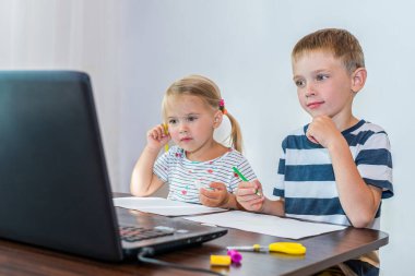 Gülümseyen çocuklar oturma odalarında online çizim dersi izliyorlar. Uzaklık öğrenimi.