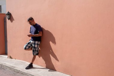 Yakışıklı adam, güneşli bir günde güneş gözlüğü takarak cep telefonunu kullanarak boş bir arkaplanda poz veriyor.