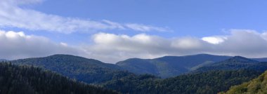 Gökyüzü ve bulutlar üzerinde ormanlarla kaplı dağlar başında