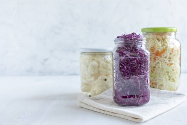 Üç beyaz zemin üzerine peçete yakın duran çeşitli nefis Fermente sebze ile kavanozlar