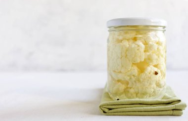 Lezzetli turşusu karnabahar ayakta beyaz arka plan üzerine kumaş parçası üzerinde kavanoz mühürlü